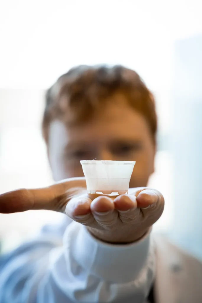 Een hand houdt een medicijnbekertje van bacteriële cellulose naar voren