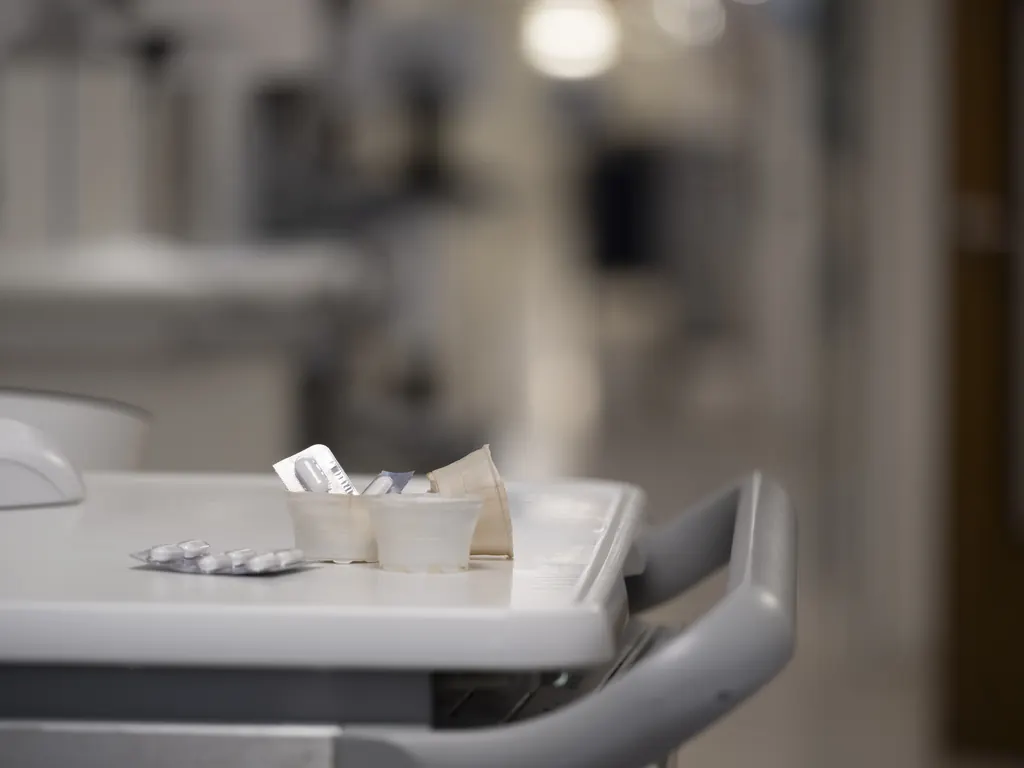 Nagespeelde foto. Medicijncupjes van cellulose op een medicijnkar in een ziekenhuisgang
